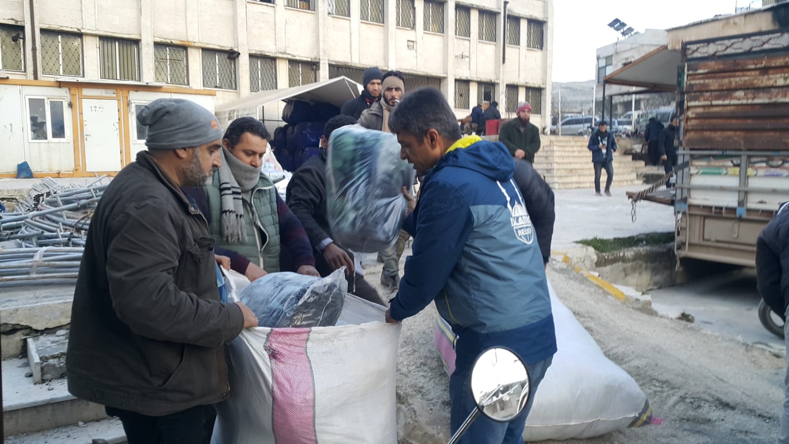 Three men are receiving bags of clothing or blankets at a loading dock in Turkey.