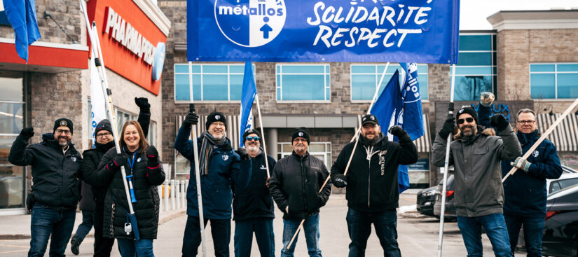 A group of Métallos at a picket, raising a flag with the slogan 